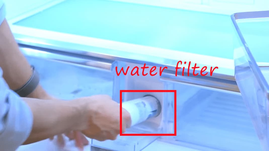 a man is pulling the water filter out from the fridge